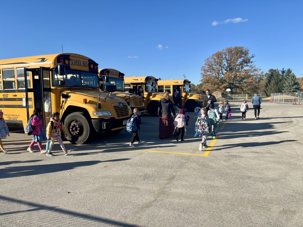students getting off of buses that are parked in a row