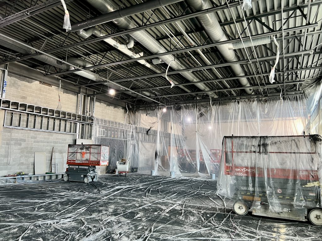 interior of Hamilton high school cafeteria addition while under construction. exposed ceiling shows progress with HVAC. much of the interior is covered in protective plastic.