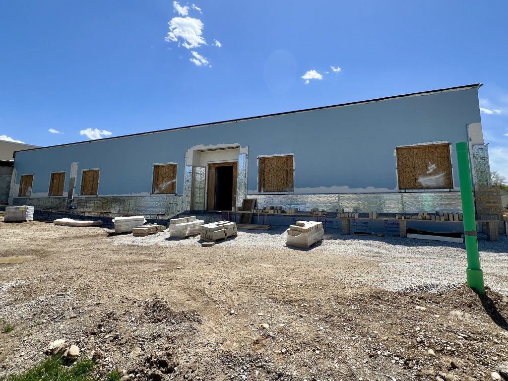 exterior of unfinished lannon addition. boarded up windows. pallets of stone lying in front. prep work being done to exterior for lannon stone veneer exterior.