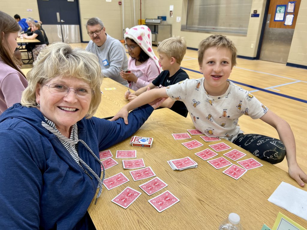 Senior volunteer with one student playing a card game.
