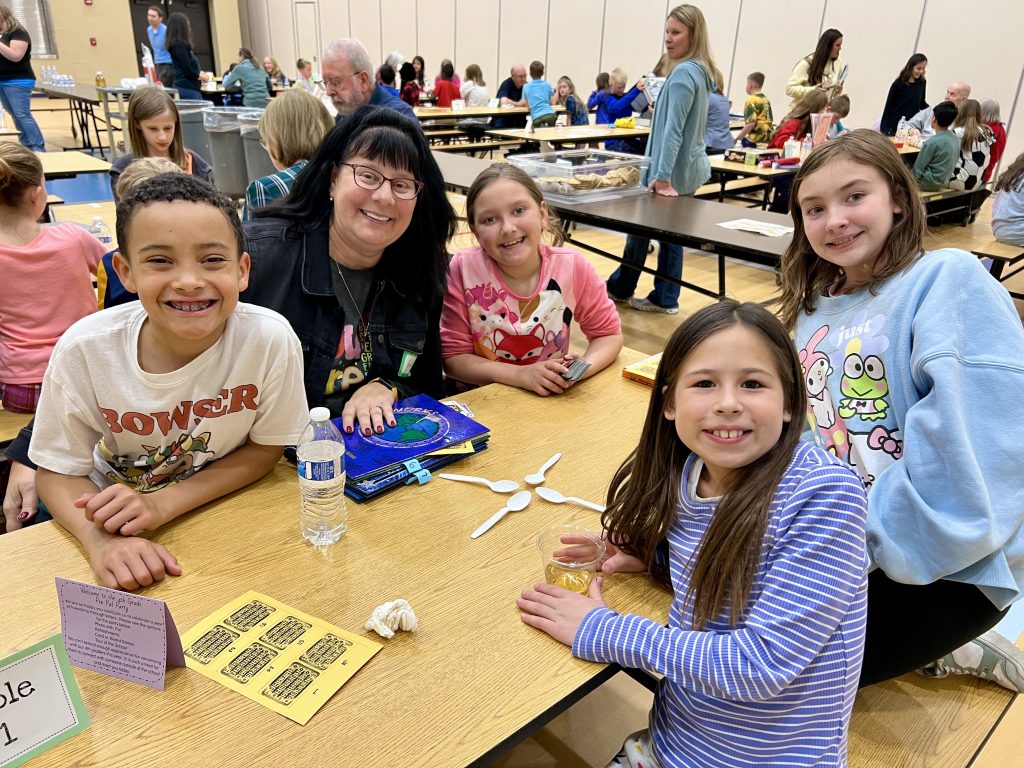 Senior Volunteer with four students smiling and playing a game.