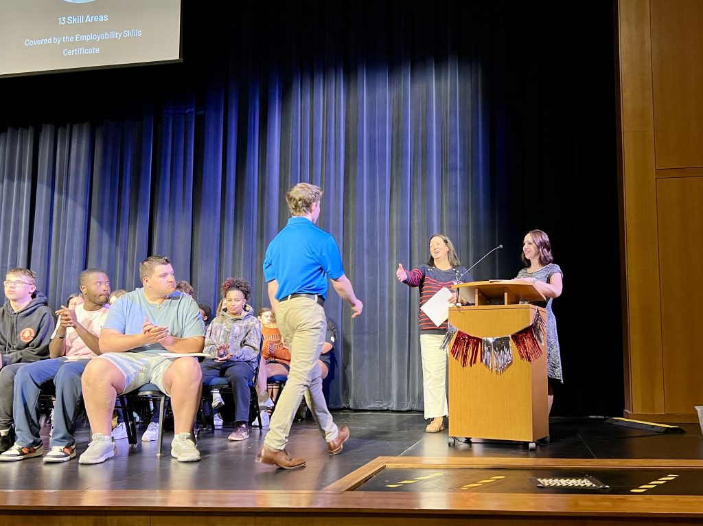 Picture of student walking toward a presenter at a podium to receive a certificate.