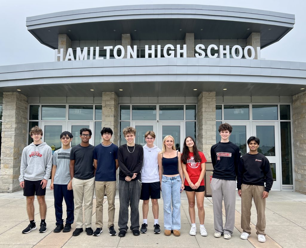 Ten high school students stand in front of their high school